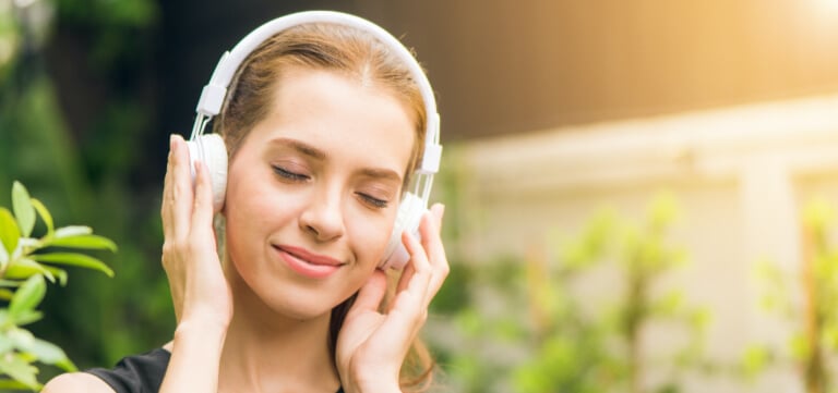 Smiling woman in park listening to audiobook on headphones